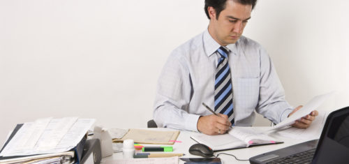 Young man working on table with computer, documents, x-ray pictures, clinical diagrams, prescriptions. Professional clinical research monitor at working place.